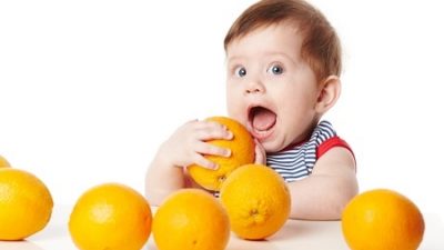 חיסכון לילדים -ילד חמוד מאוד משתעשע עם תפוזים כתומים על רקע לבן