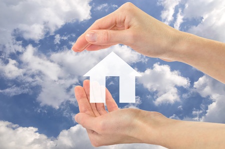 צורה של בית בצבע לבן בין מרחפת בין שתי כפות ידיים המגוננות עליה ובקרע שמיים כחולים עם עננים ושדה ירוק