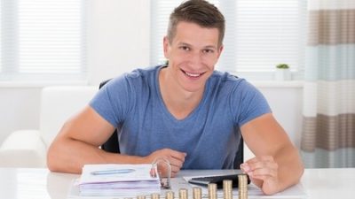 בחור צעיר יושב מאחורי שולחן ומתבונן בדוחות קרן השתלמות שלו ומטבעות זהב מסודרות לפניו בסדר עולה.