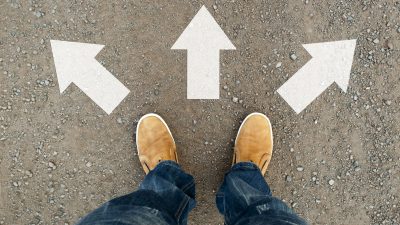 אדם נועל מגפיים צהובות ועומד על הכביד היכן מסומנים חצים לבחירה לאן כדאי לו ללכת - ניוד ביטוח מנהלים
