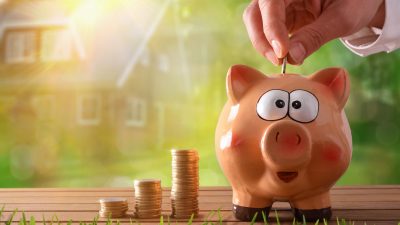 יד של אדם משלשל מטבע לקופת חיסכון ומתלבט היכן לנהל את החיסכון שלו בחברת ביטוח או בבנק